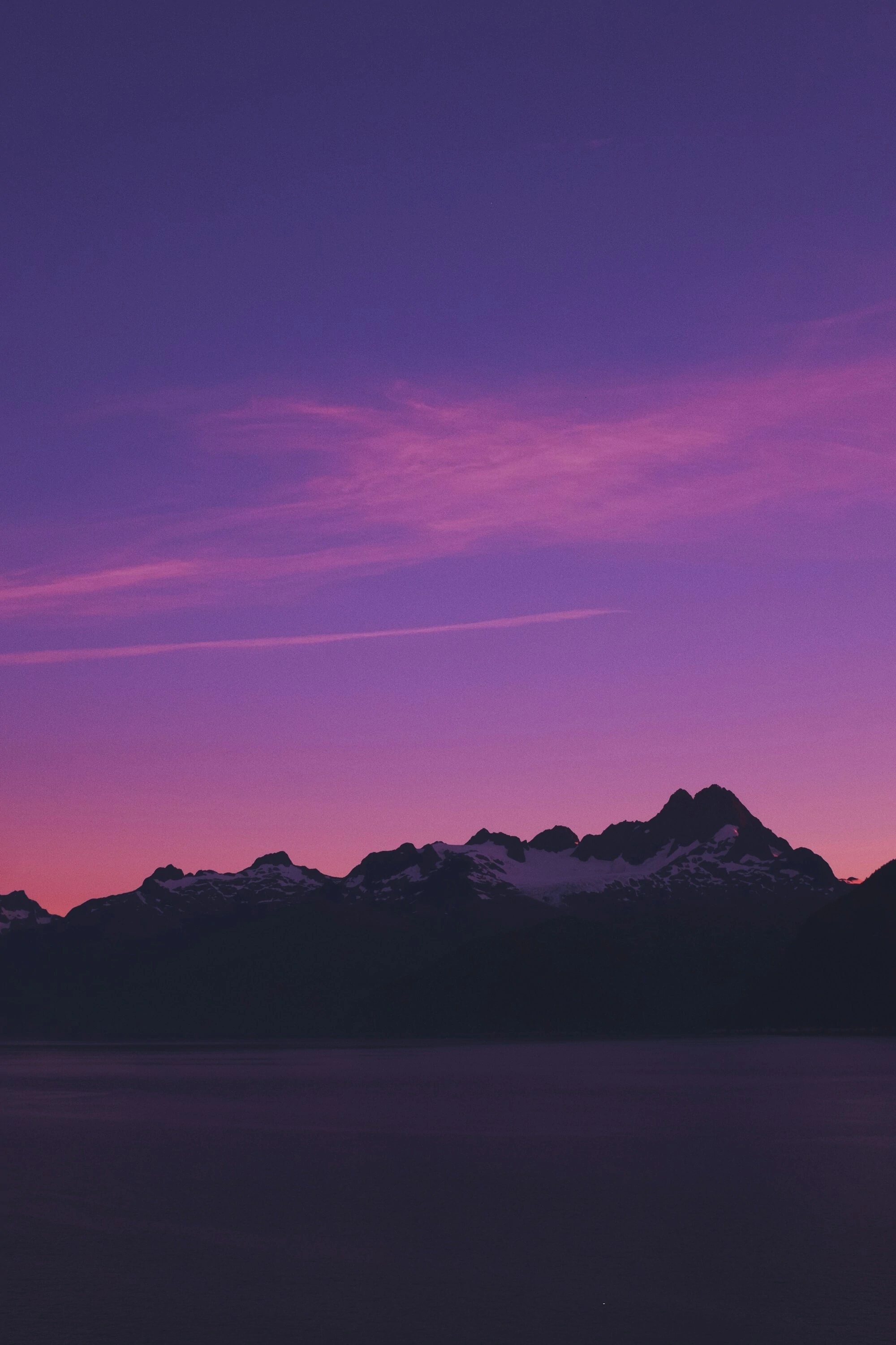 The beautiful silhouette of a mountain located in the Pacific Northwest. The sunset behind it is colored with vibrant hues of purple, pink, and dark blue.
